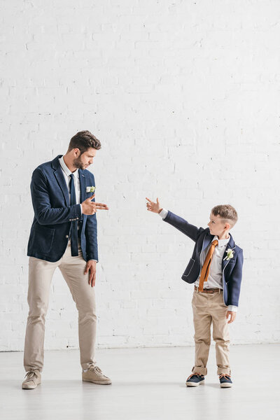 full length view of father and son in jackets with boutonnieres looking at each other