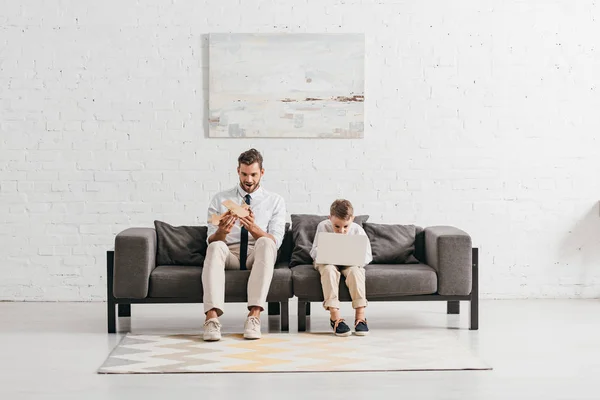 Ayah Dengan Mainan Pesawat Dan Anak Dengan Laptop Duduk Sofa — Stok Foto