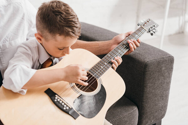 cropped view of dad teaching son to play acoustic guitar at home