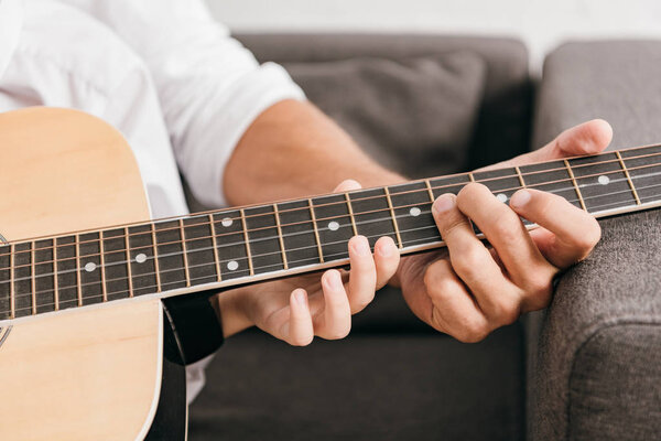 cropped view of dad teaching son to play acoustic guitar at home