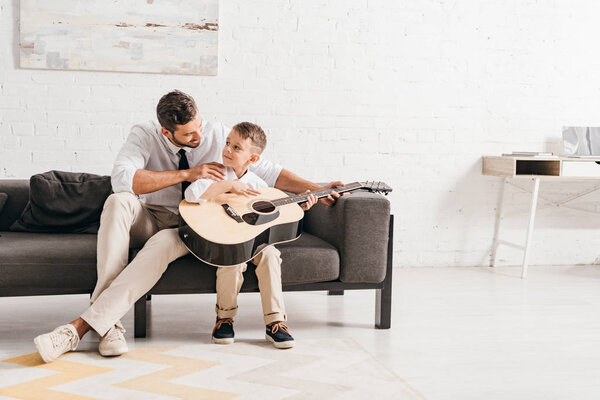 dad teaching son to play acoustic guitar at home