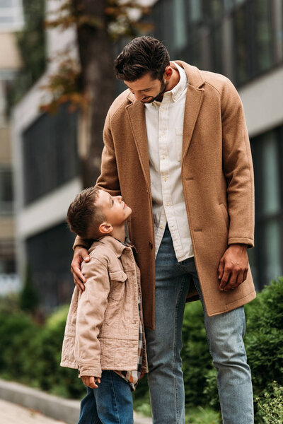 happy father and son embracing and looking at each other on street