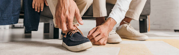 panoramic shot of father tying shoelaces to son