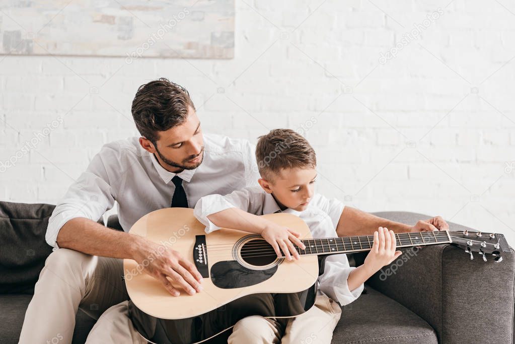 dad teaching son to play acoustic guitar at home