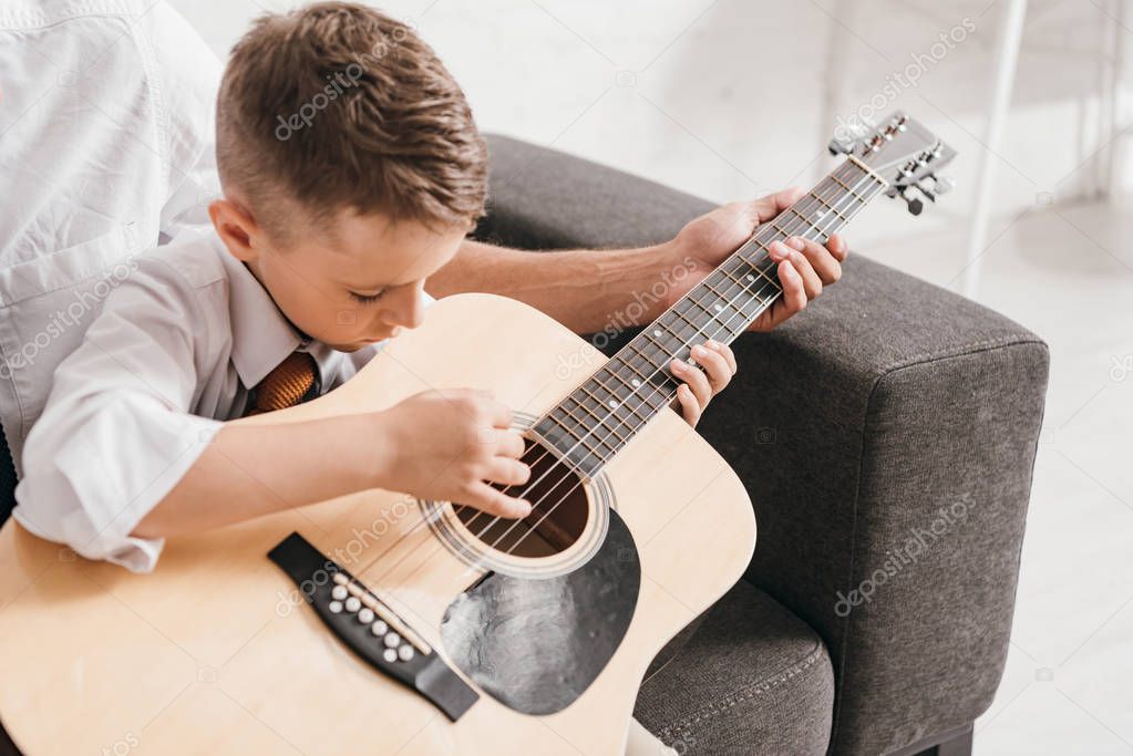 cropped view of dad teaching son to play acoustic guitar at home