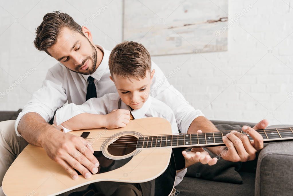 dad teaching son to play acoustic guitar at home