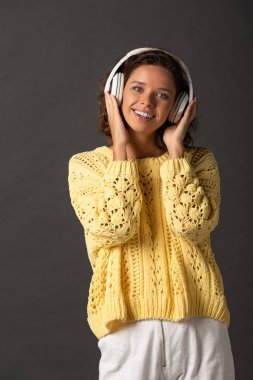 siyah arka plan üzerinde kulaklık müzik dinleme sarı örme kazak gülümseyen kıvırcık kadın
