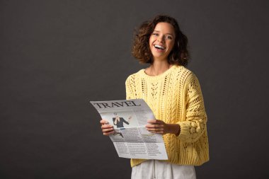 sarı örme kazak siyah arka plan üzerinde seyahat gazetesi tutan mutlu kıvırcık kadın