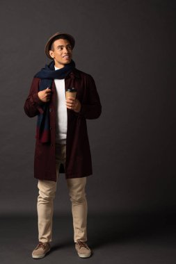 siyah arka plan üzerinde kağıt bardak tutan eşarp ve şapka gülümseyen karışık yarış adam