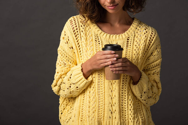 cropped view of woman in yellow knitted sweater holding coffee to go on black background