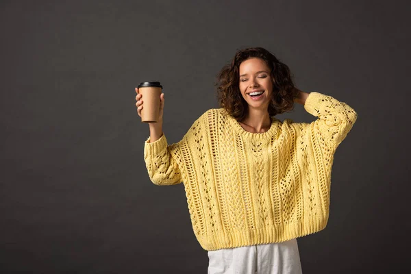 快乐卷发的女人在黄色针织毛衣与闭着眼睛拿着咖啡去黑色背景 — 图库照片