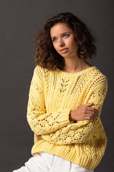dreamy curly woman in yellow knitted sweater on black background