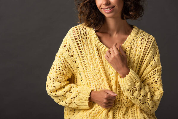 partial view of smiling curly woman in yellow knitted sweater on black background