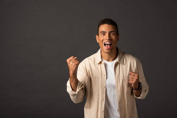 excited handsome mixed race man in beige shirt showing yes gesture on black background