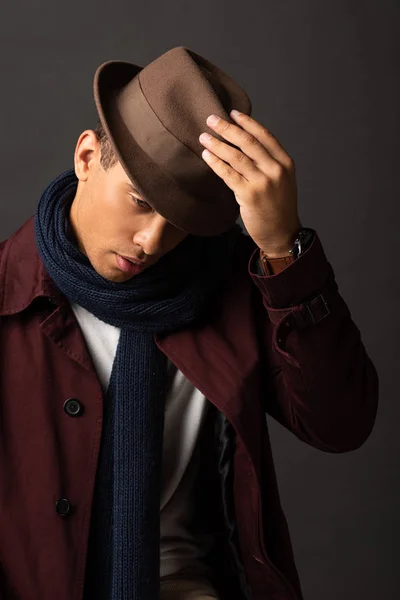 mixed race man in scarf holding hat on black background