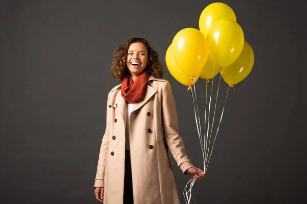 Happy Curly Woman Trench Coat Holding Yellow Balloons Black Background — Stock Photo, Image