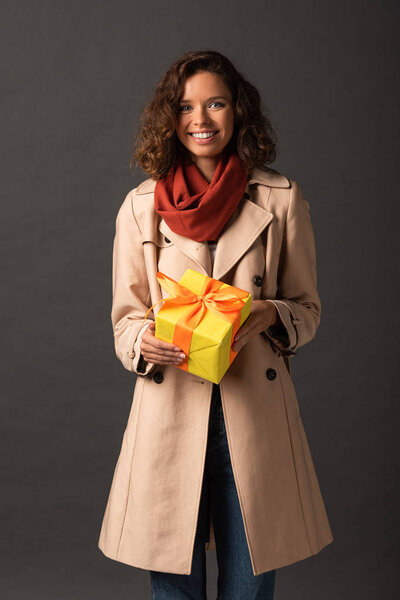 smiling woman in trench coat holding present on black background