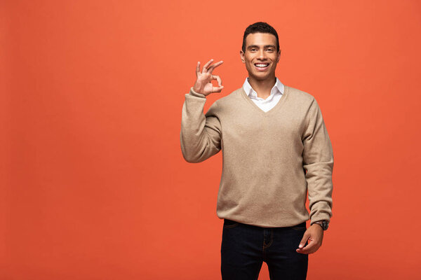 счастливый мужчина смешанной расы в бежевом свитере с оранжевой табличкой
