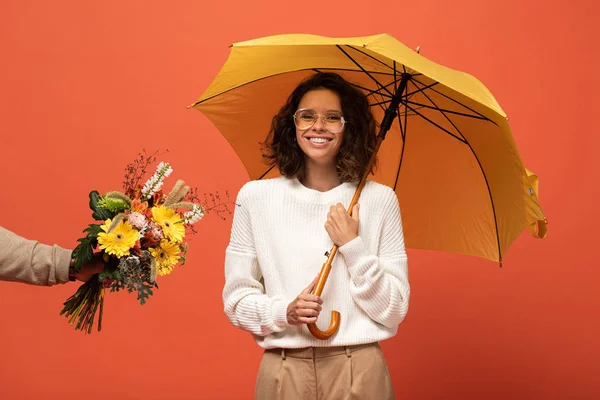 オレンジ色に隔離された花の傘の花束を持つ幸せな女性を贈るボーイフレンド — ストック写真