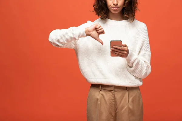 裁剪视图的妇女在秋天的服装使用智能手机和显示拇指向下孤立的橙色 — 图库照片