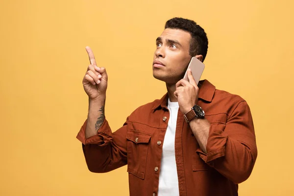 Pensive Mixed Race Man Talking Smartphone Pointing Finger Isolated Yellow — Stock Photo, Image