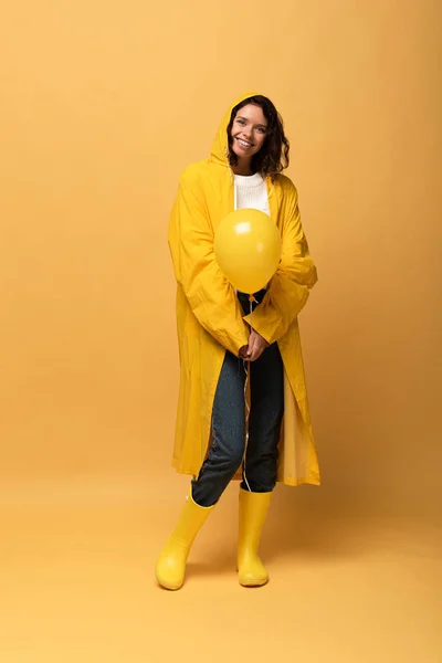 Smiling Curly Woman Yellow Raincoat Wellies Holding Balloon Yellow Background — Stock Photo, Image
