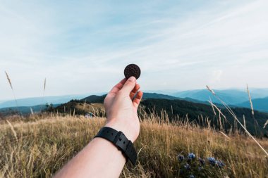 Karpatlar, Ukrayna - 24 Ağustos 2019: dağların yakınındaki tarlada oreo kurabiye tutan adamın kırpılmış görünümü 