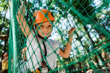 selective focus of happy kid in helmet with safety equipment in adventure park  clipart