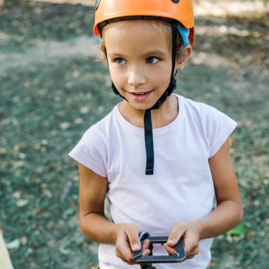 happy kid in helmet holding safety equipment outside clipart
