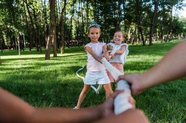 selective focus of cheerful multicultural children competing in tug of war outside  clipart