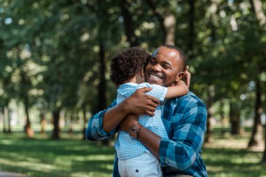 happy african american father with closed eyes hugging curly son  clipart