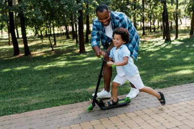 cheerful african american father near happy kid on scooter  clipart