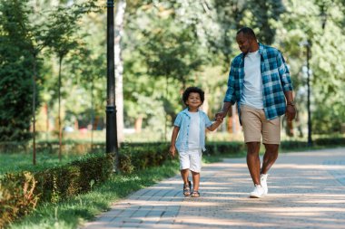 happy african american boy holding hands while walking with father  clipart
