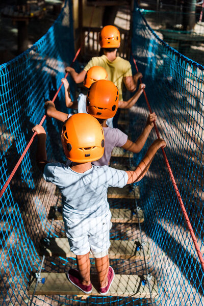 back view of four multicultural kids in helmets in adventure park 