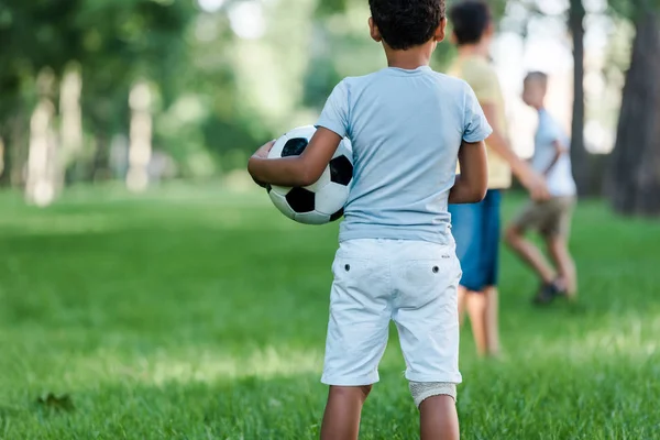 back view of african american child standing with football near boys 