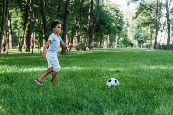 adorable african american child playing football on green grass 