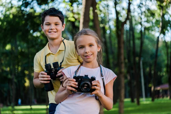 快乐的男孩拿着双筒望远镜 带着数码相机在公园里接近他的朋友 — 图库照片