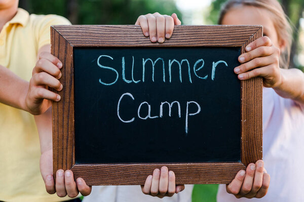 cropped view of kids holding chalk board with summer camp letters 
