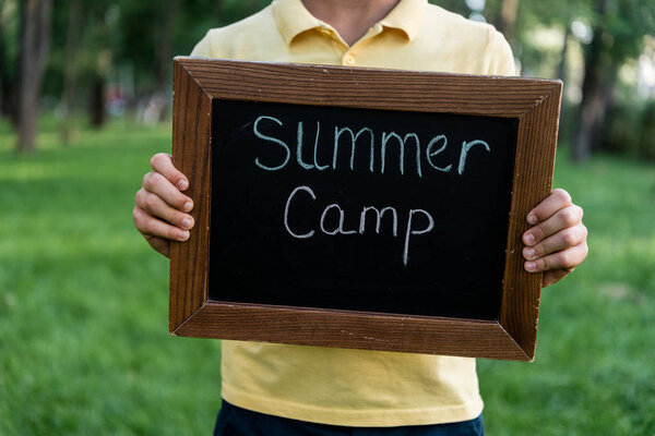 cropped view of boy holding chalk board with summer camp letters 