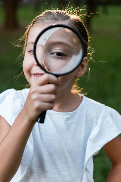 selective focus of cheerful kid holding magnifier near eye 
