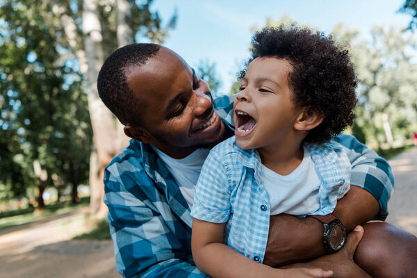 happy african american man hugging positive kid in park 