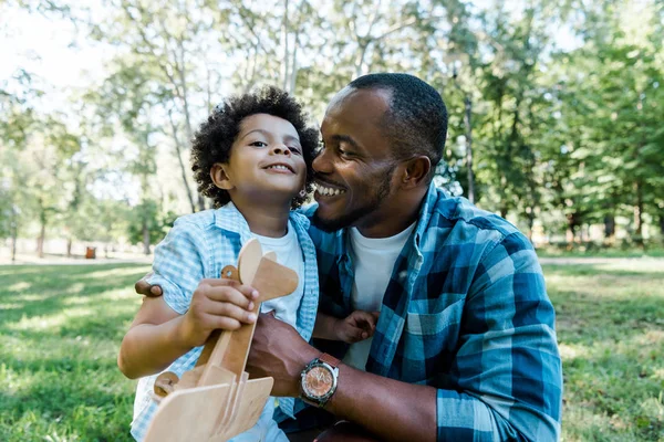 Glücklich Afrikanisch Amerikanischer Vater Schaut Niedlichen Sohn Mit Holzspielzeug Doppeldecker — Stockfoto