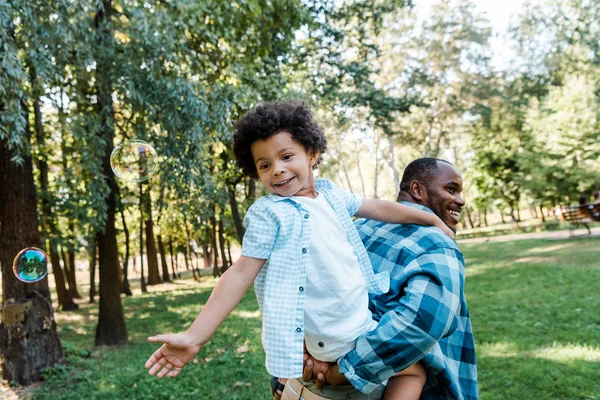 African American Piggybacking Cute Curly Son Soap Bubbles Park — Stock Photo, Image