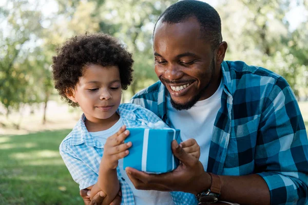 Fröhlich Afrikanisch Amerikanischer Vater Und Sohn Betrachten Blaue Geschenkschachtel — Stockfoto