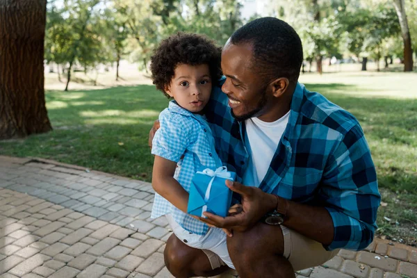 Happy African American Man Holding Blue Gift Looking Curly Son — Stock Photo, Image