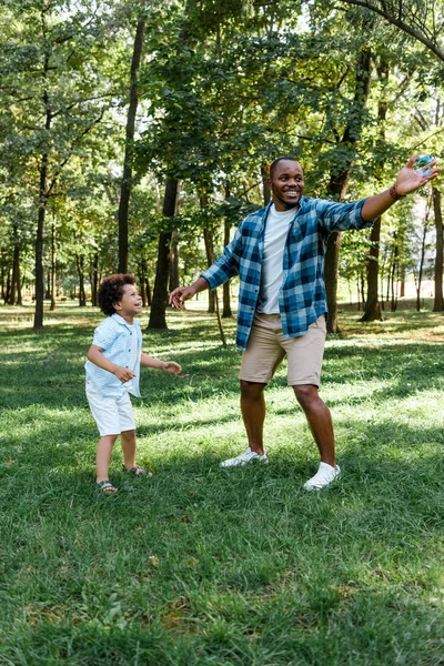 公園の草の上に立っている幸せなアフリカ系アメリカ人の父と息子 — ストック写真