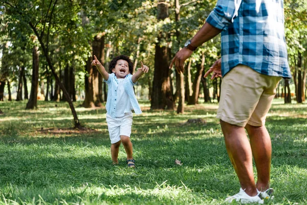 公園で指を指差すかわいいアフリカ系アメリカ人の子供の近くに立っている父親のトリミングされたビュー — ストック写真
