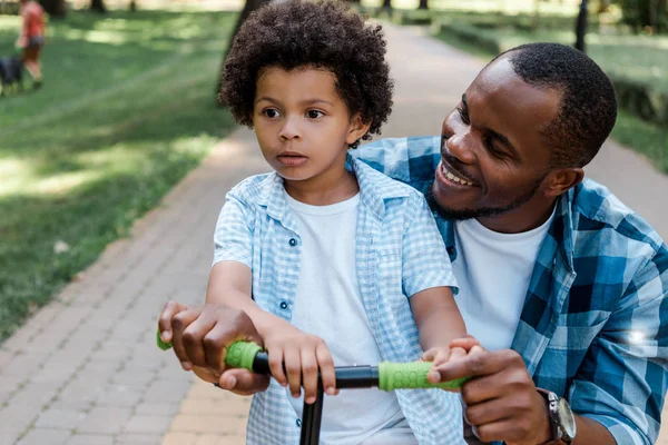 mutlu afrikalı amerikalı baba kıvırcık çocuk scooter sürme bakıyor 