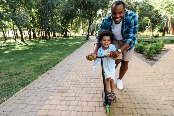 Glimlachend Afro Amerikaanse Vader Buurt Van Schattige Zoon Rijden Scooter — Stockfoto