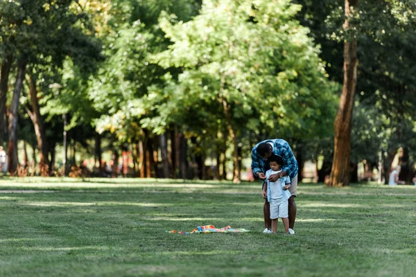 草の上にかわいい息子の近くに立っているアフリカ系アメリカ人の父親 — ストック写真